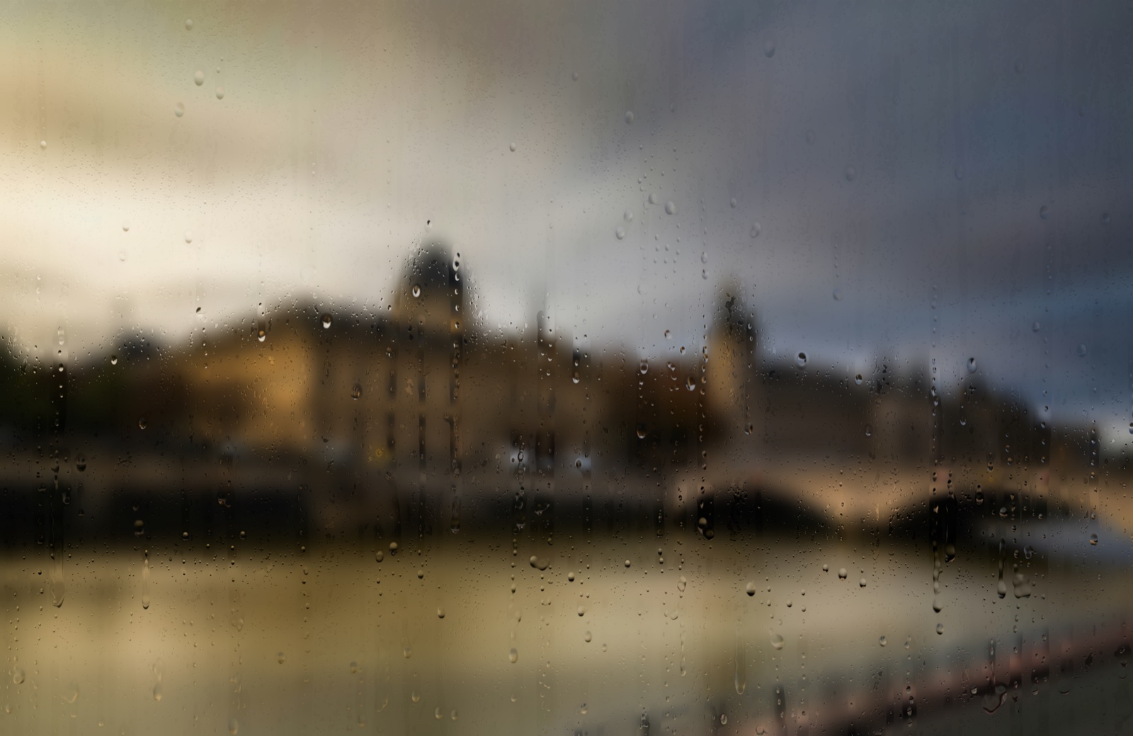 Rain on glass over the Seine at golden hour: warm sky, the Conciergerie's domes catching the last light, the river still beneath them.